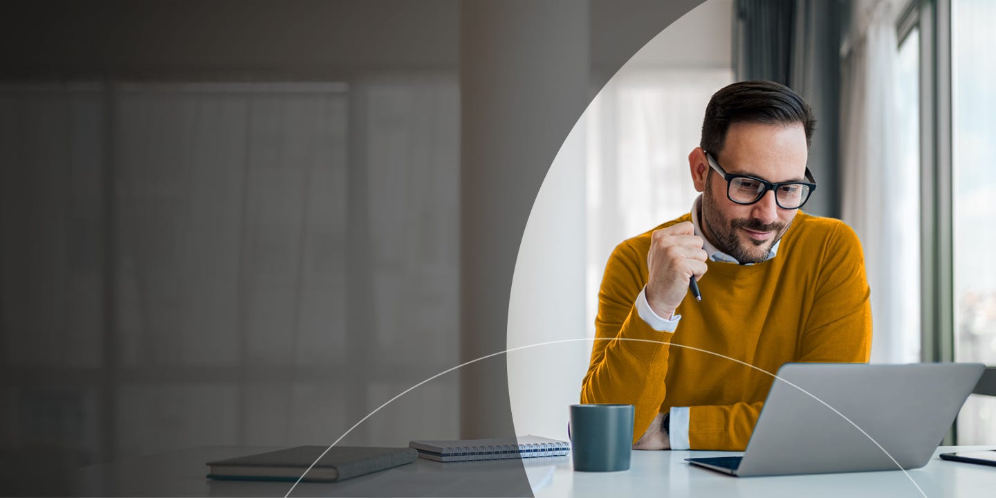 Man holding a pen and looking at a laptop.
