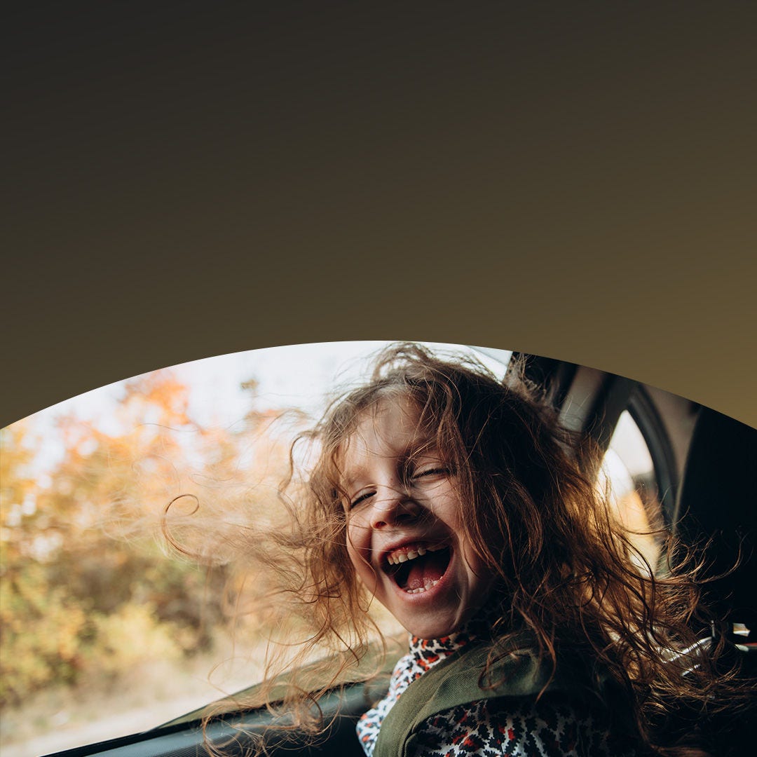 Child with long hair laughing joyfully in the back seat of a car