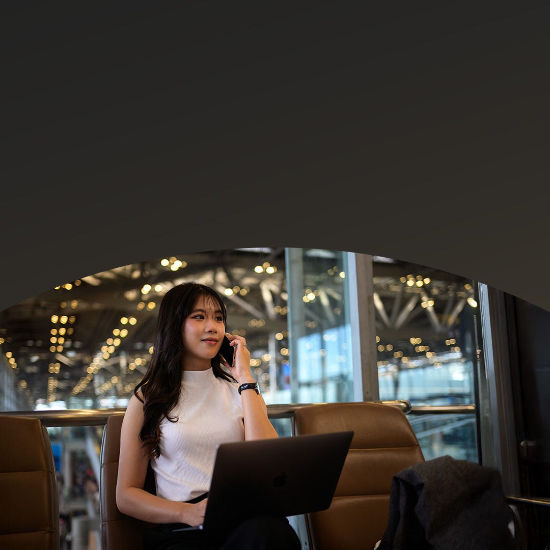 A woman multitasking on her laptop and phone call while seated in the lounge, awaiting her boarding call.