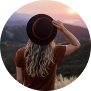 woman holding her hat facing a sunset
