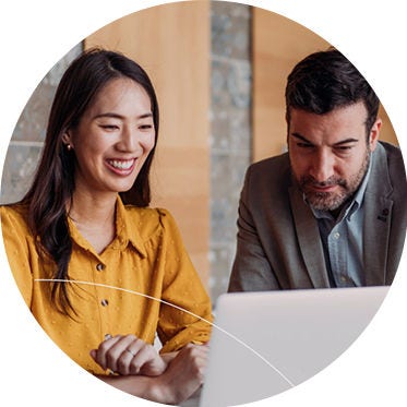 A man and woman collaborate on a laptop, focused on their work in a modern office setting.