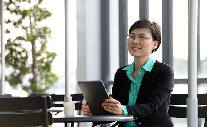 Woman in office smiling with tablet in hand.