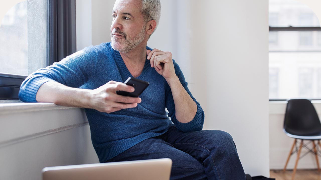 Man gazing out of the window, holding a mobile phone