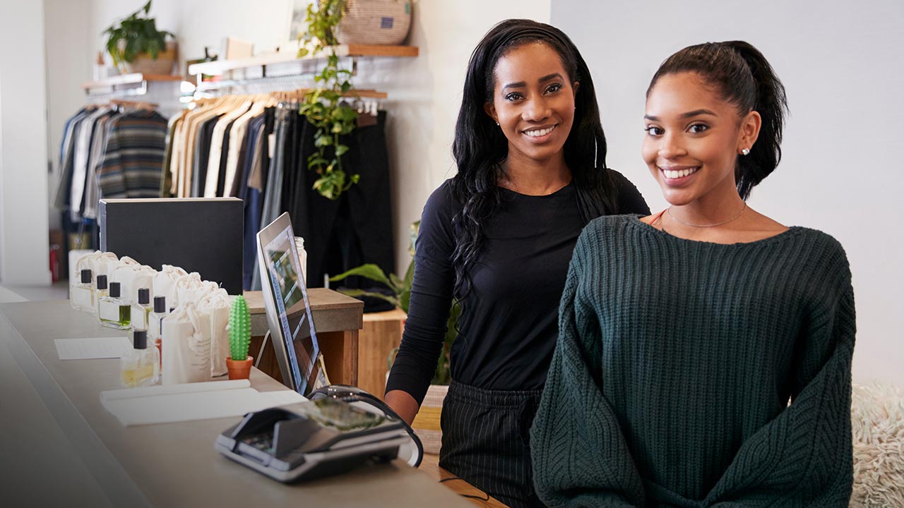 Two women smiling behind the counter in clothing store.