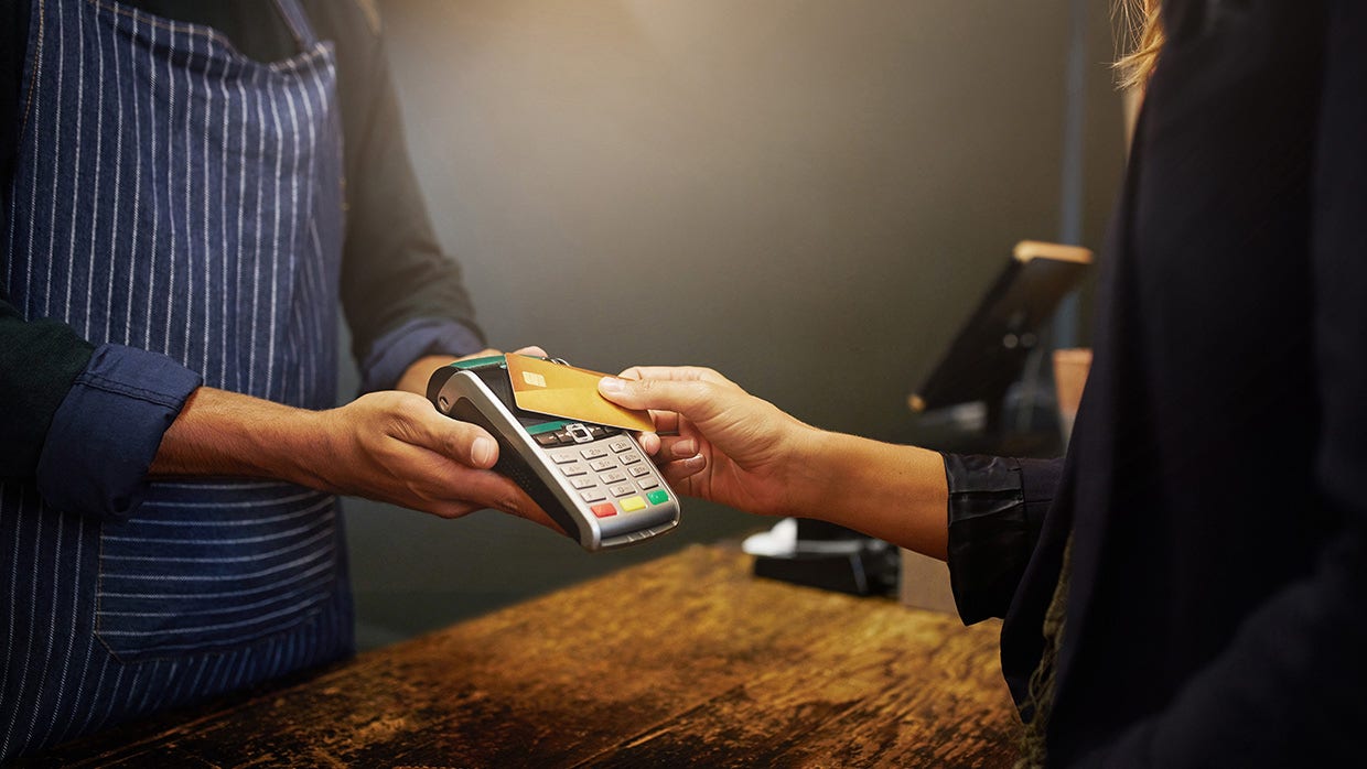 A person taps their card on a payment terminal, indicating a transaction in progress.