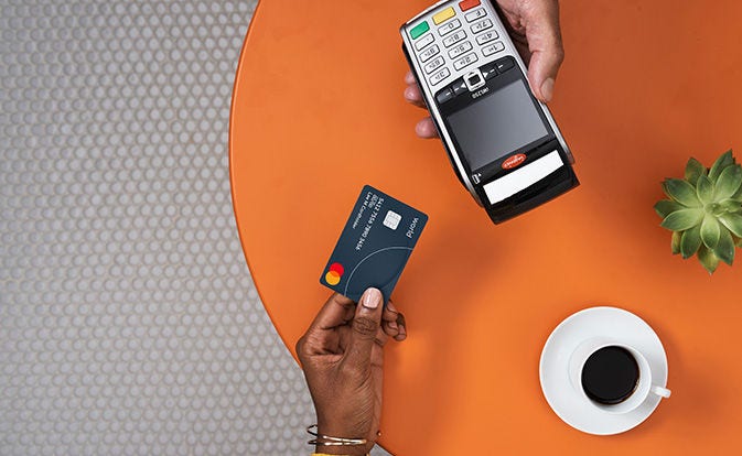 Customer holding a Mastercard, ready to pay with a POS terminal at a café table.