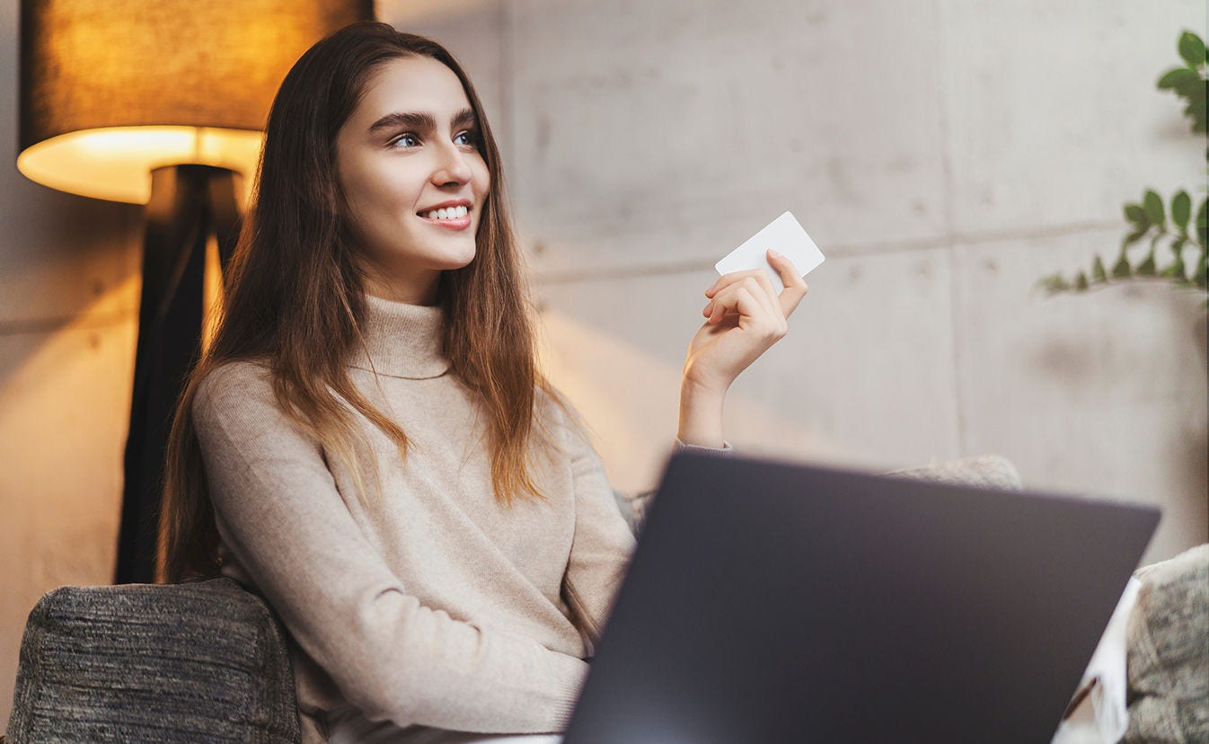 Woman holds payment card while sitting in front of laptop