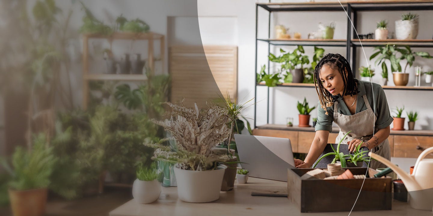 A woman focused on her laptop, surrounded by various plants in a vibrant plant shop.