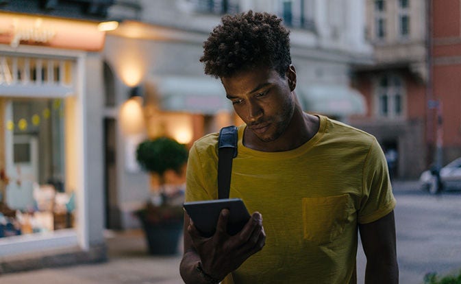A man wearing a yellow shirt gazes at his phone, seemingly engaged with its content.