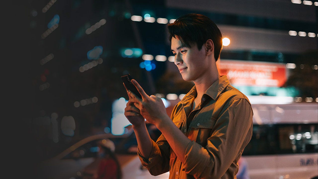Man is using his phone while walking on the street at night.