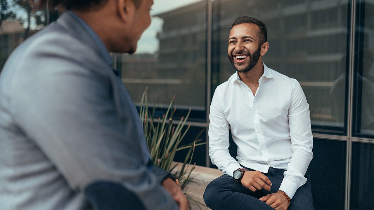 Two trendy businessmen talking and laughing casually outside
