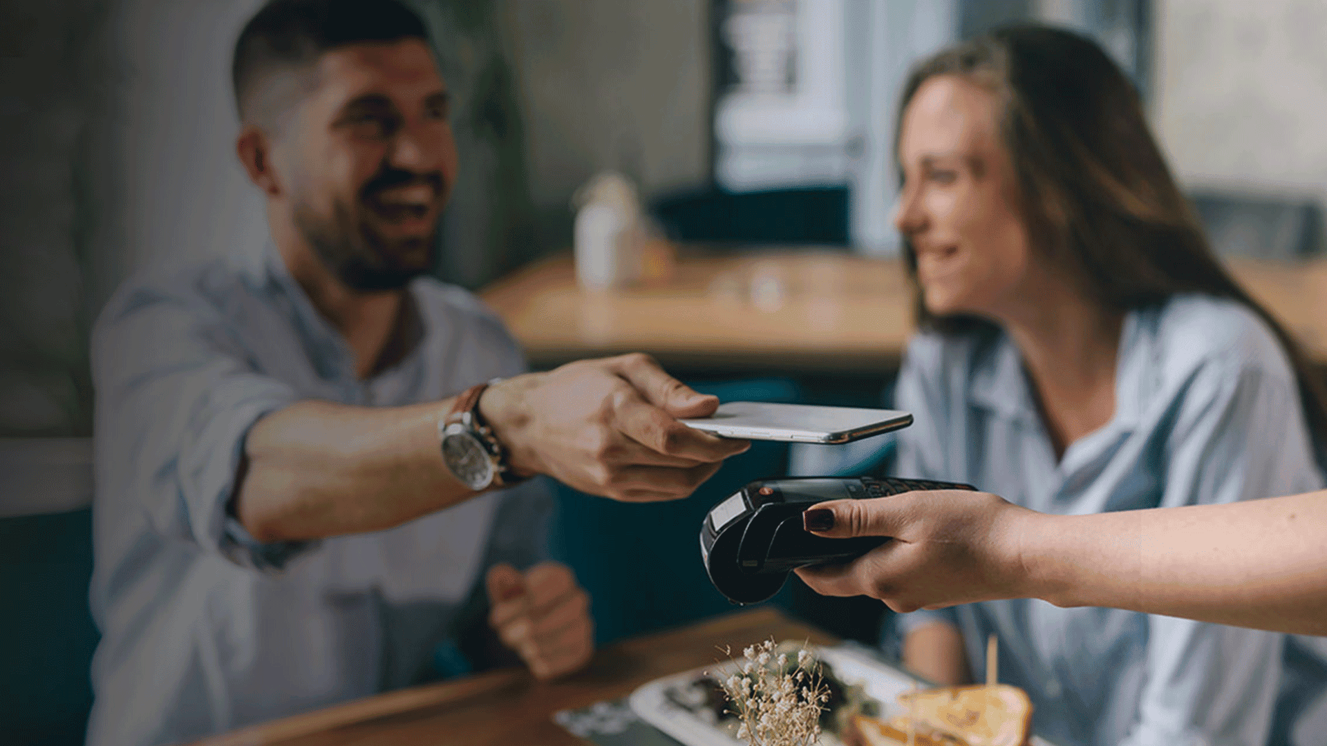 Man paying for food with mobile phone sitting next to woman