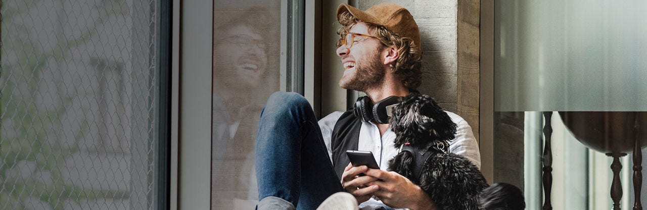 Smiling man sitting next to a window with phone in hands