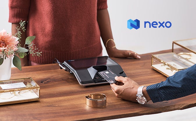An individual is making a payment at a jewelry store using a cryptocurrency card via a card reader placed on the counter.