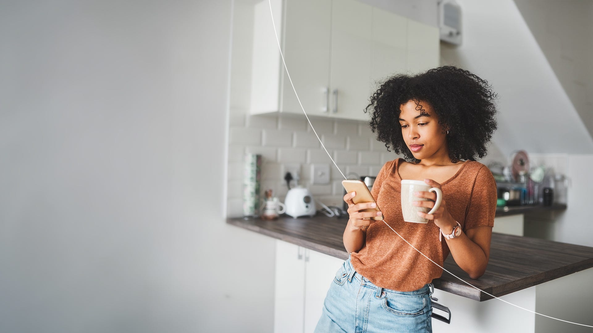 woman standing in kitchen on smartphone holding a cup.