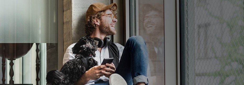 Man with dog and phone in hand looking through window