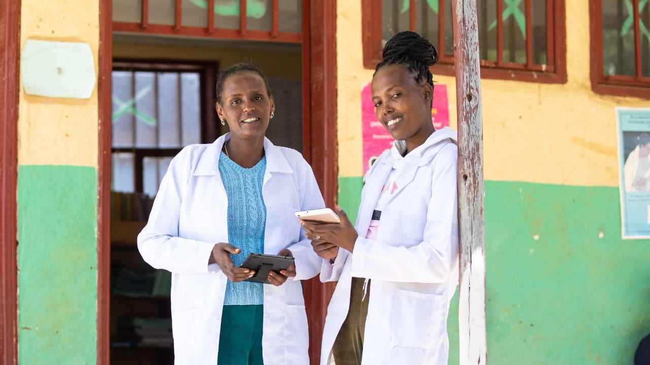 Two community health workers in Ethiopia hold tablets outside a clinic. 