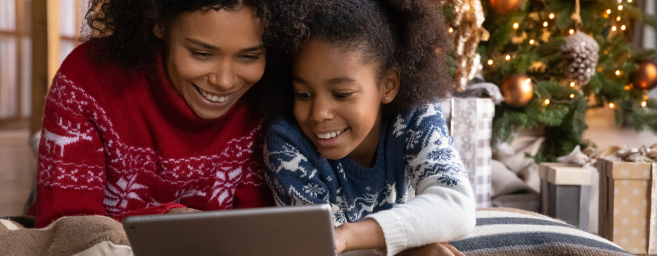 A mother and daugher look at a tablet with a Christmas tree in the background