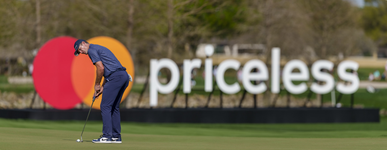 Justin Rose lines up a shot on the green in front of a Mastercard logo and Priceless sign. 