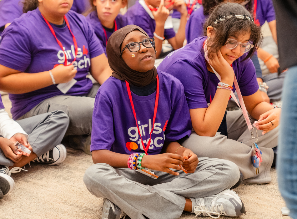 A girl in a Girls4Tech T-shift looks up toward an instructor during a cybersecurity exercise. 