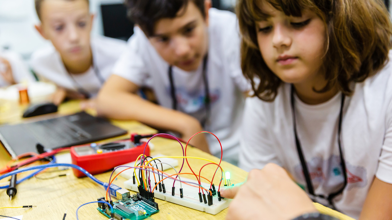 Three kids examine a circuit board. 