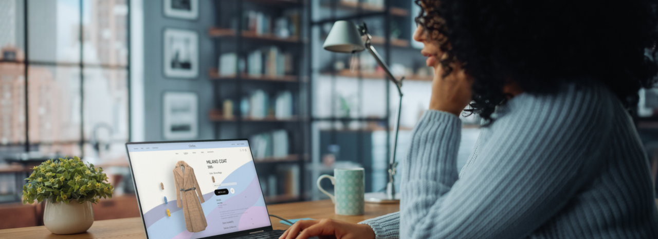 A woman sits a desk looking at an online shopping site. 